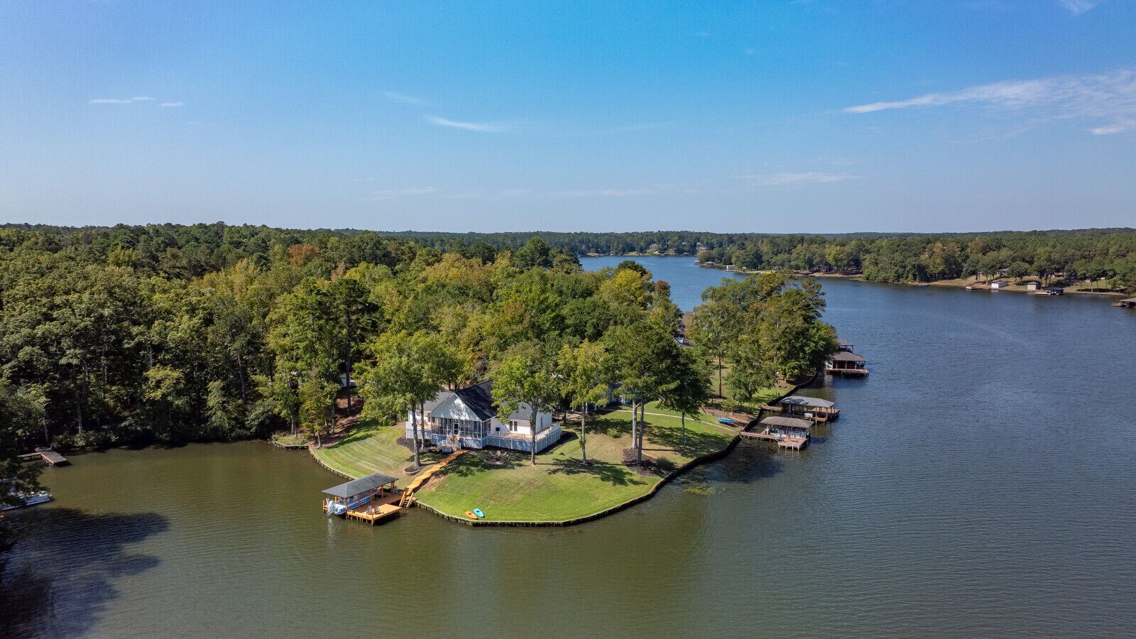 Una propiedad junto al lago con una casa rodeada de árboles, barcos amarrados y una vista despejada del lago.