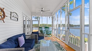 Eine überdachte Veranda mit Seeblick, möbliert mit Korbstühlen und einer Couch.