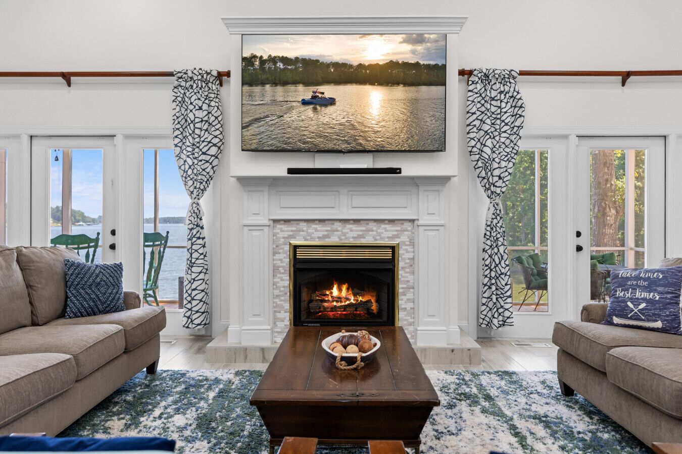 A living room with a fireplace, a television mounted above it, and a view of a lake through large windows.
