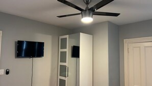 Ein Zimmer mit Deckenventilator, Wandfernseher und einer Tür.