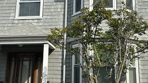 Ein zweistöckiges Haus mit grauer Fassade, weißen Fenster- und Türrahmen sowie einem kleinen Baum im Vorgarten.