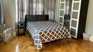 Ein Schlafzimmer mit Bett, Schrank, Nachttisch, Ventilator und einem Fenster mit Vorhängen.