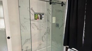 Ein Duschbereich mit Glaswänden, einer Wand aus Marmorfliesen und einer Glastür.