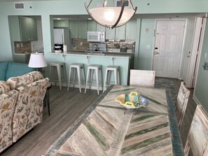 A modern kitchen with a central island, bar stools, and a dining table with a decorative centerpiece. - Long Beach Resort 4-1203 2-bedroom condo all new! Easy access & great views. (Panama City Beach)