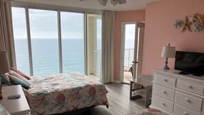 Ein Schlafzimmer mit Bett, Sofa, Fernseher, Kommode und einem Balkon mit Meerblick.