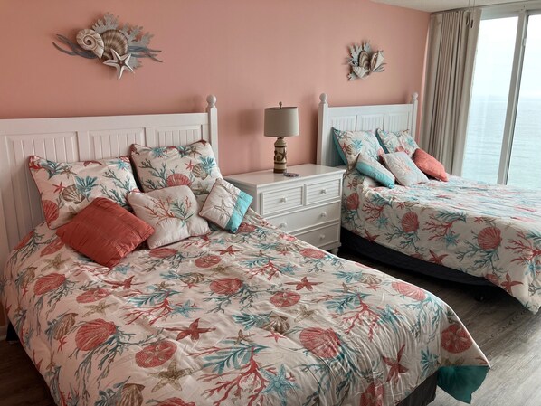 Un dormitorio con dos camas, una mesita de noche, detalles decorativos en la pared y vistas al mar.