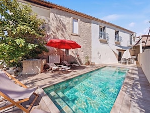 Un espace piscine avec des chaises longues, un parasol rouge et un mur en pierre.