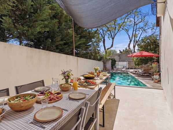 Un espace extérieur aménagé pour les repas, avec une piscine, entouré d’arbres et d’un mur de pierres.