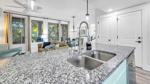 A modern kitchen with granite countertops, stainless steel sinks, and a dining area with a sofa and table. - 1 bed/2 bath, walk to Baytowne! Quick tram ride to beach! (Miramar Beach)