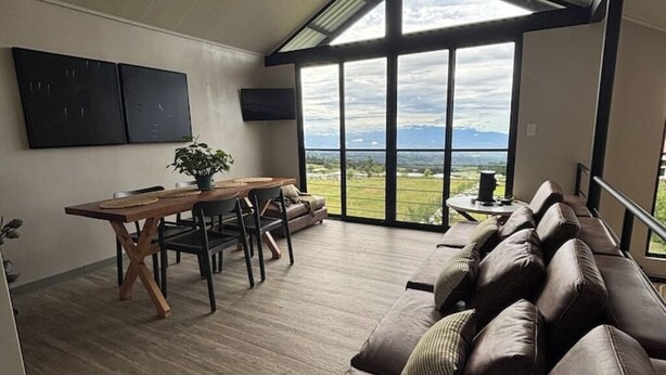 A spacious room with a dining area, a sofa, and a large window offering a view of the outdoors.