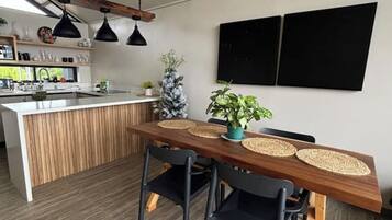 Uma cozinha moderna com uma ilha de madeira, luminárias pendentes pretas e uma área de jantar com mesa e cadeiras de madeira, ambas pretas.