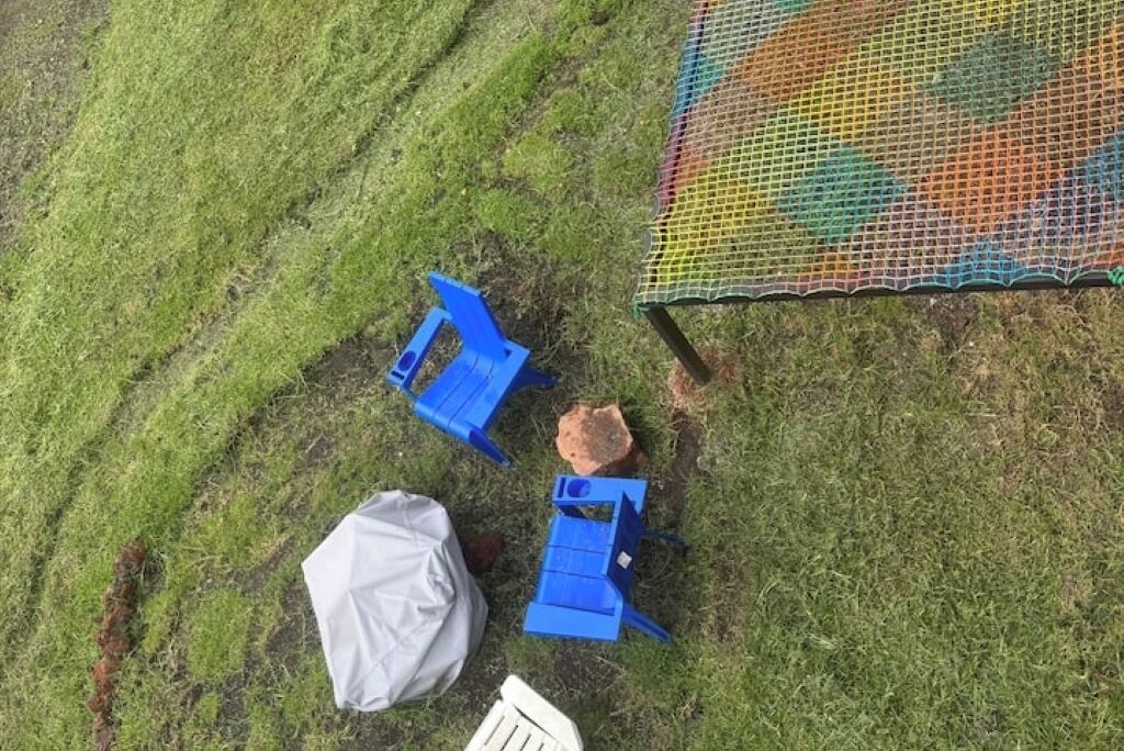 Een gazon met blauwe stoelen en een wit object, mogelijk een tas, vlakbij een kleurrijke, omheinde constructie.