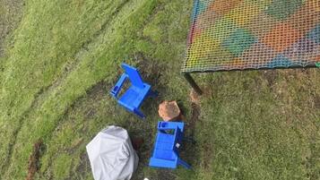 Een gazon met blauwe stoelen en een wit object, mogelijk een tas, vlakbij een kleurrijke, omheinde constructie.