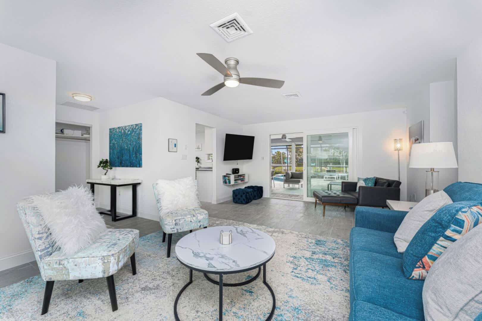 Un salon moderne doté d’un ventilateur de plafond, d’un téléviseur et d’une grande fenêtre donnant sur l’extérieur.