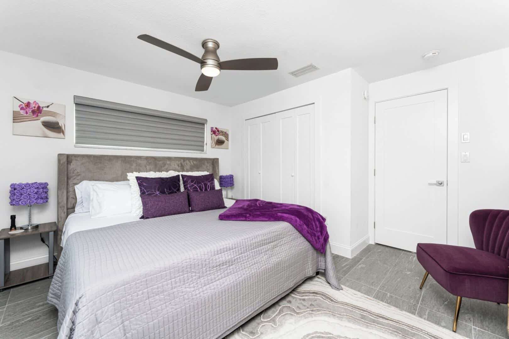 Un dormitorio con una cama, un ventilador de techo, una mesita de noche, una silla y una puerta.