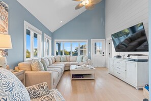 A spacious living room with a large sectional sofa, a flat-screen TV, and a ceiling fan. - Hills By The Sea – The Ultimate 8-Bedroom Luxury Beach Retreat (Sleeps 20!) (Ocean Isle Beach)