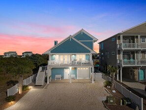 Ein zweistöckiges Strandhaus mit Balkon, einer überdachten Garage und einer Auffahrt zum Eingang.