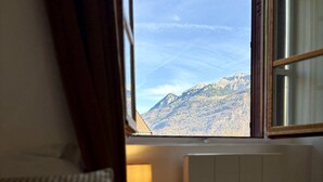 Habitación de hotel con cama, lámpara de noche, radiador y ventana con vistas a la montaña.