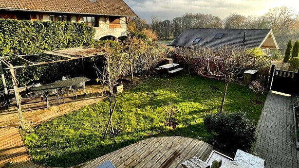 Una terraza de madera con una mesa y sillas, rodeada de un jardín y vistas a montañas al fondo.