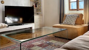 Una sala de estar moderna con un televisor de pantalla plana, una mesa de centro de vidrio, un tapete estampado y un sofá con cojines decorativos.