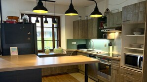Cocina moderna con armarios de madera, horno empotrado, microondas y un lavamanos. Hay dos taburetes y lámparas colgantes sobre la encimera.