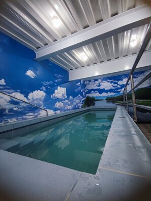 Piscina interior com um mural no teto retratando um céu azul e nuvens.