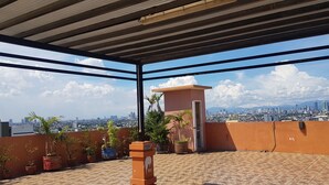 A rooftop terrace with potted plants, a water hose, and a view of a cityscape with mountains in the background. - Modern Oasis - Cozy Loft Condo in Manila (Manila)