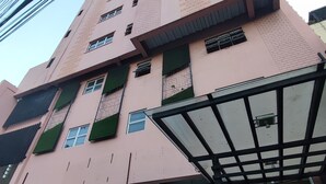 A tall pink building with multiple windows and air conditioning units. There is a covered entrance with a car parked in front. - Modern Oasis - Cozy Loft Condo in Manila (Manila)