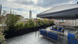 Eine Dachterrasse mit überdachter Sitzecke, Blumentöpfen und Blick auf die Stadt.