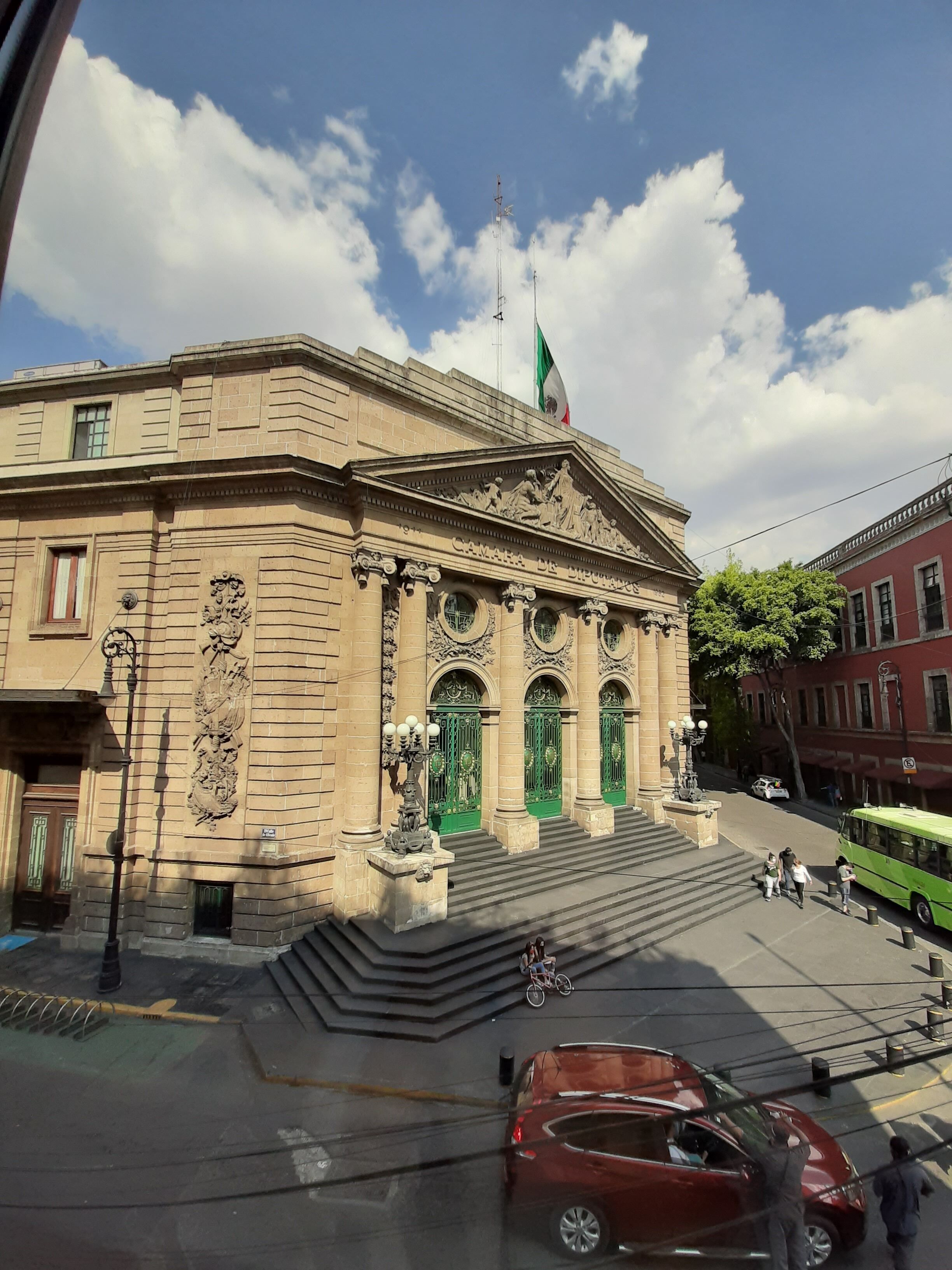 A historic building with classical architecture, featuring a prominent entrance with green doors and a flag.