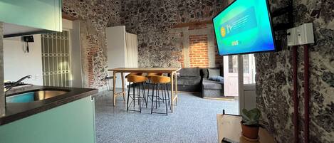 A modern kitchen with a stone wall backdrop, a dining area with bar stools, and a flat-screen TV mounted on the wall.