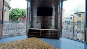 Ein Zimmer mit einem großen, strukturierten Teppich, einem an der Wand befestigten Fernseher und Blick auf die Stadt durch große Fenster.