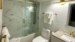 Une salle de bain dotée d’une douche à parois de verre, de toilettes, d’un lavabo avec un robinet doré et d’un miroir au-dessus du lavabo.
