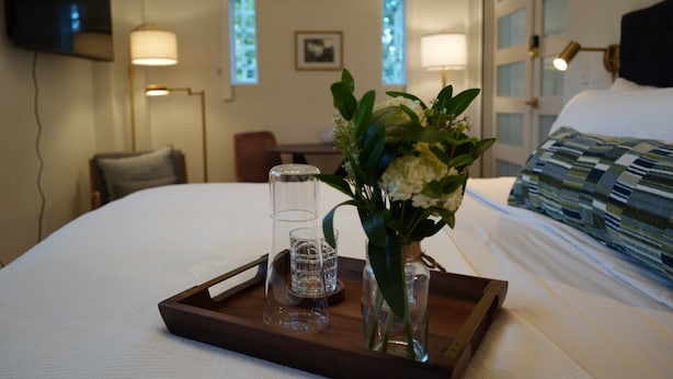 Un lit bien fait, avec un plateau de verres et un vase de fleurs.
