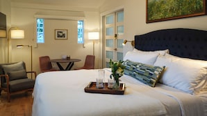 Une chambre d’hôtel avec un grand lit, une petite table, deux chaises, un tableau et une fenêtre donnant sur un beau paysage.