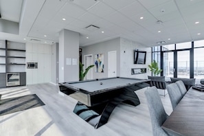 Een moderne pooltafel in een ruimte met een bank, stoelen, een televisie en een groot raam met uitzicht op de stad.