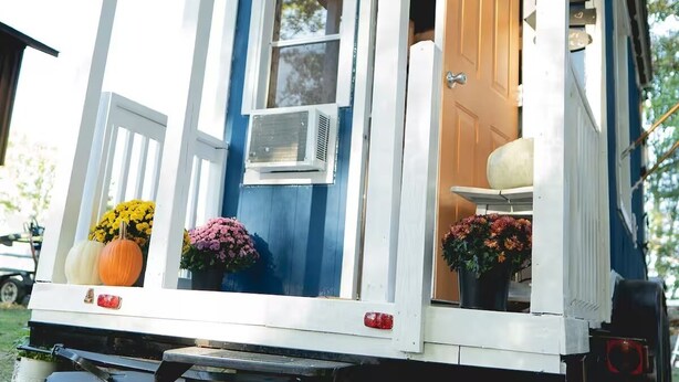 Een stacaravan met een veranda, een schuifdeur en een raam met een airconditioning.