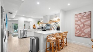 Una cocina moderna con armarios blancos, una isla central con taburetes altos y un salpicadero con diseño geométrico.