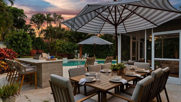 Un área de comedor al aire libre con piscina, bar y sillones de descanso.