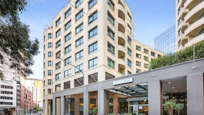 Um hotel moderno com entrada central, vários andares e fachada de vidro.