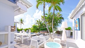Un espace aménagé au bord de la piscine, avec des meubles blancs, un jacuzzi et des palmiers.