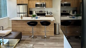 Une cuisine moderne avec des meubles en bois, des appareils en acier inoxydable, un îlot central doté de tabourets de bar et un grand téléviseur à écran plat.