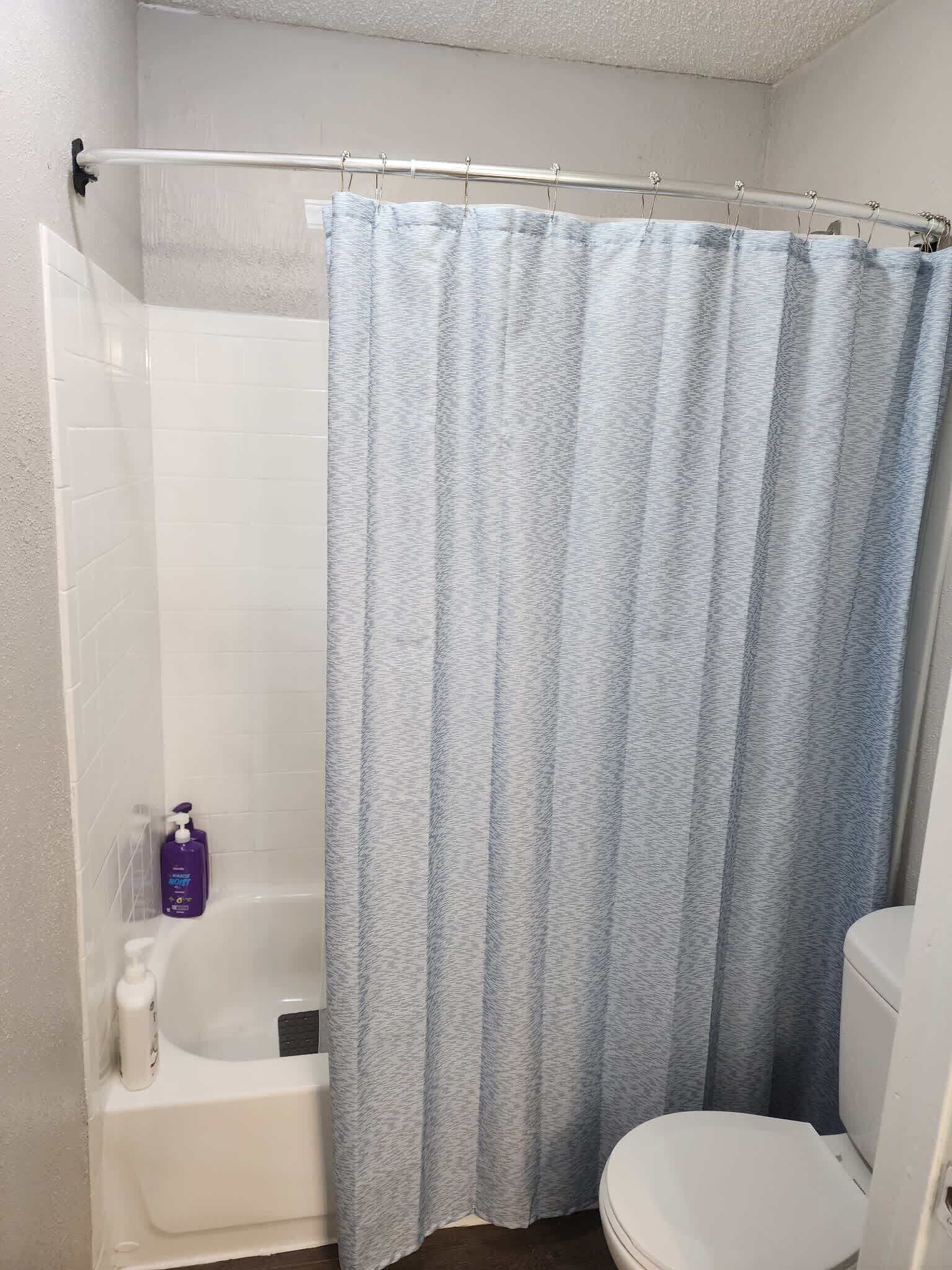 A bathroom with a shower curtain, a bathtub, and a toilet.