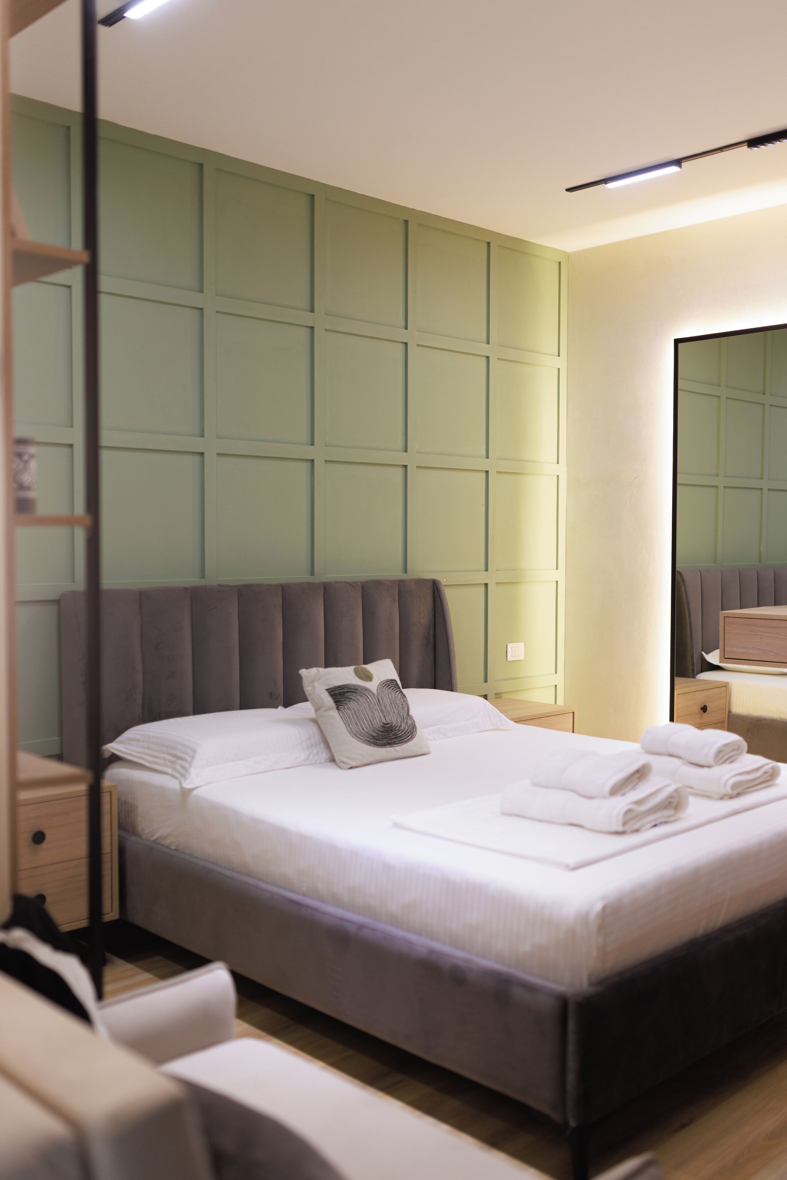 A modern hotel room with a large bed, a bedside table, a nightstand, and a mirror.