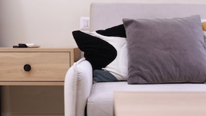 Een moderne kamer met een lichtgekleurde bank, een houten nachtkastje en een klein tafeltje.
