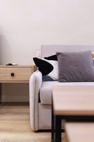 Una habitación moderna con un sofá de color claro, una mesita de noche de madera y una pequeña mesa.