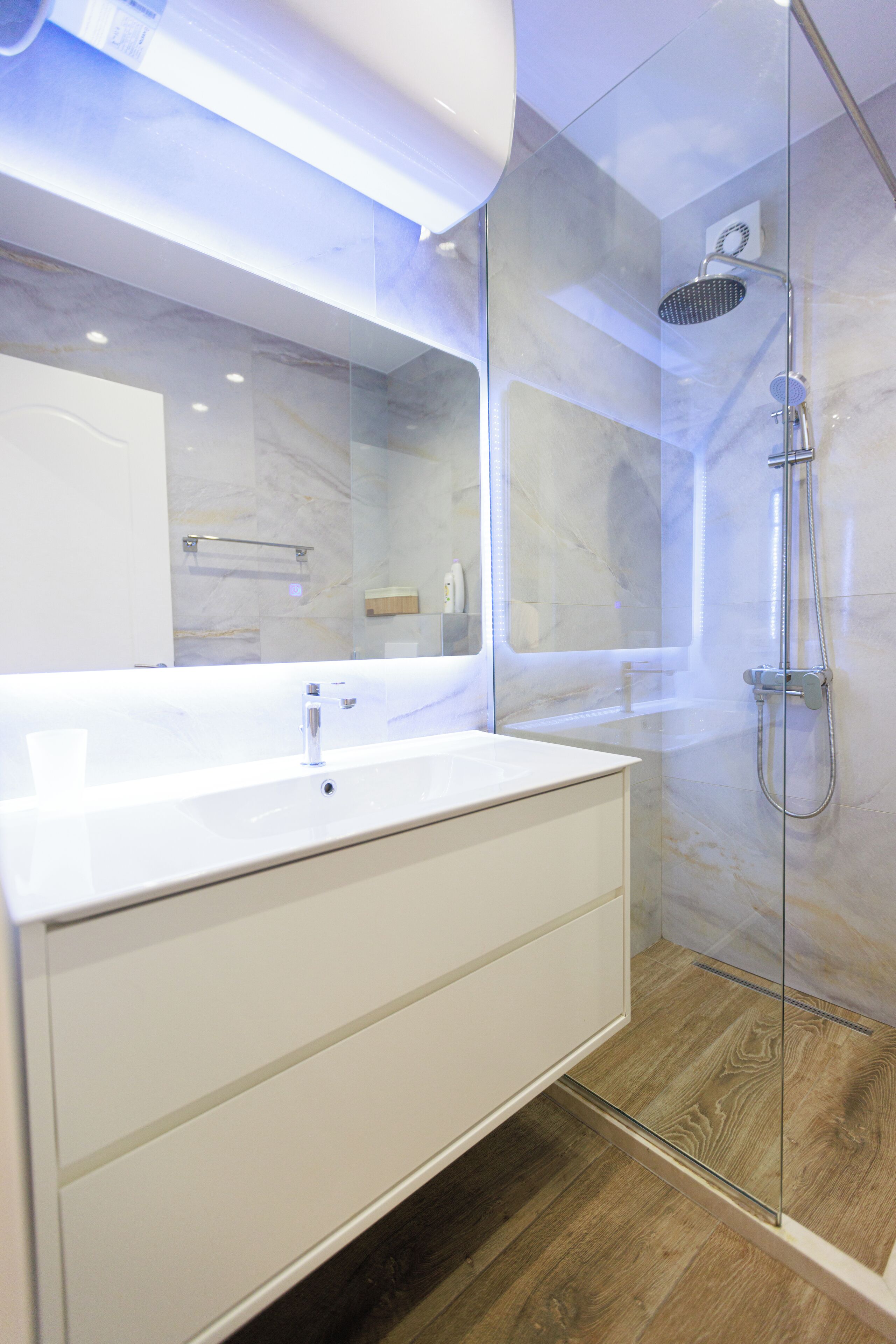 Une salle de bain moderne avec une douche à parois de verre, un meuble-lavabo blanc doté d'un grand miroir et des murs en marbre.