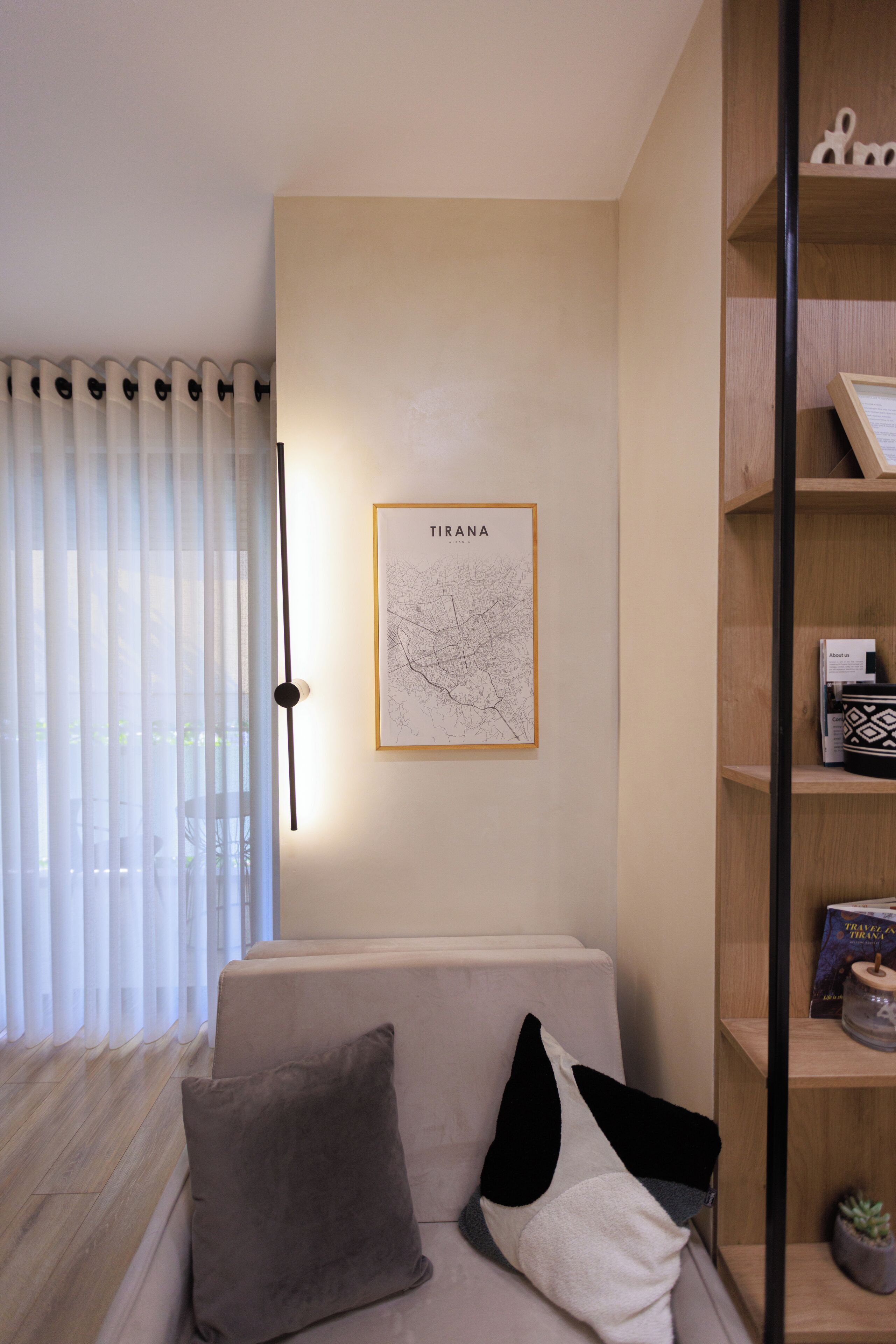 Un salon moderne avec un canapé, une carte de Tirana et une bibliothèque en bois.
