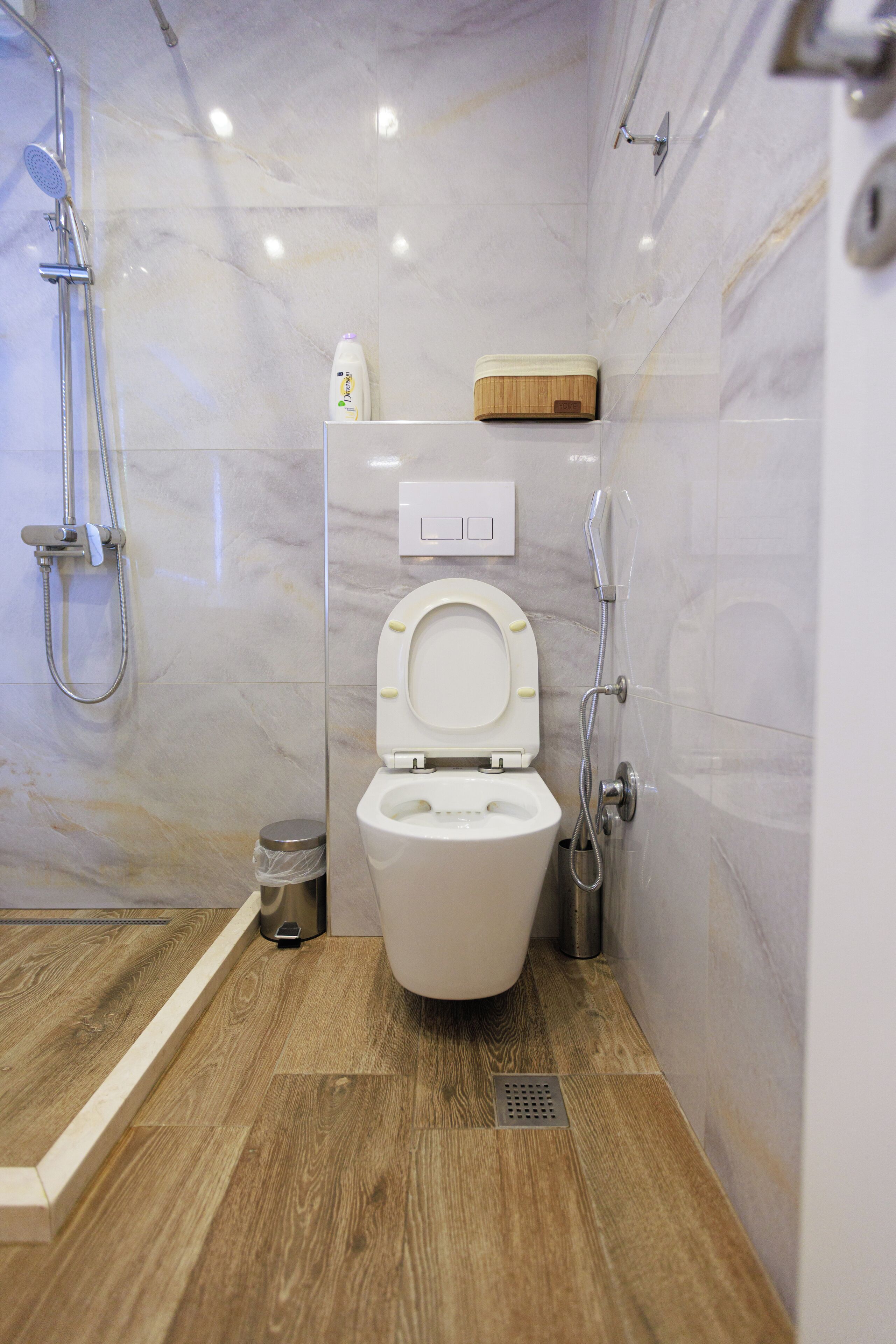 A modern bathroom with a toilet, shower, and a wooden floor.