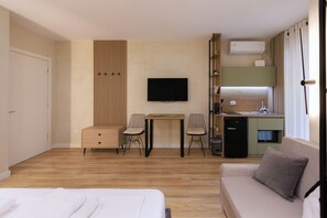 Moderni hotellihuone, jossa on sänky, sohva, työpöytä ja kaksi tuolia, televisio, minijääkaappi, mikroaaltouuni ja sisäänrakennettu ilmastointilaite.